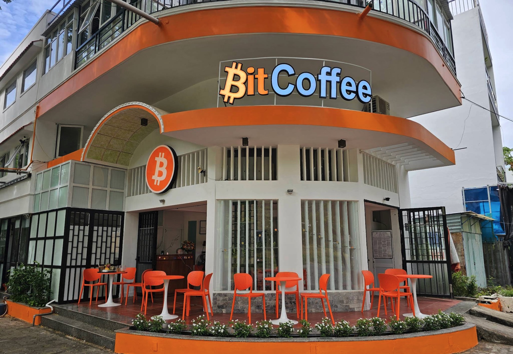 ₿itCoffee storefront with the orange BitCoffee sign and Bitcoin logo, outdoor seating with orange chairs